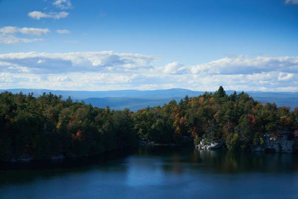 Lake Minnewaska and the surrounding landscape show the beginnings of fall colors in the trees on a sunny day with bright blue sky and low white clouds