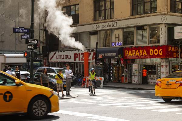 A busy New York intersection showing restaurants, taxis, pedestrians, and an e-bike rider