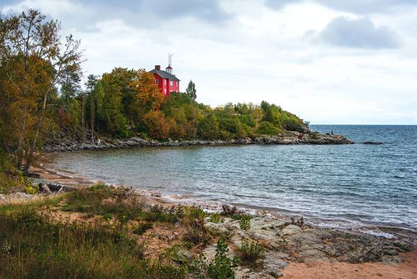 Bright red building behind colorful early-autumn trees on a rocky Michigan coastline, below cloudy skies