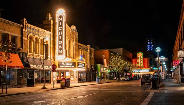 Nighttime street scene with empty sidewalks and empty streets, featuring brightly lit exterior of a theater; theater sign reads "MICHIGAN"