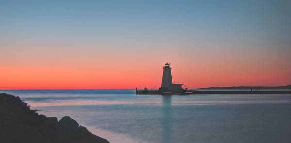 A red, pink, and orange sunset with a clear sky and view of a pier and lighthouse in Ludington, Michigan