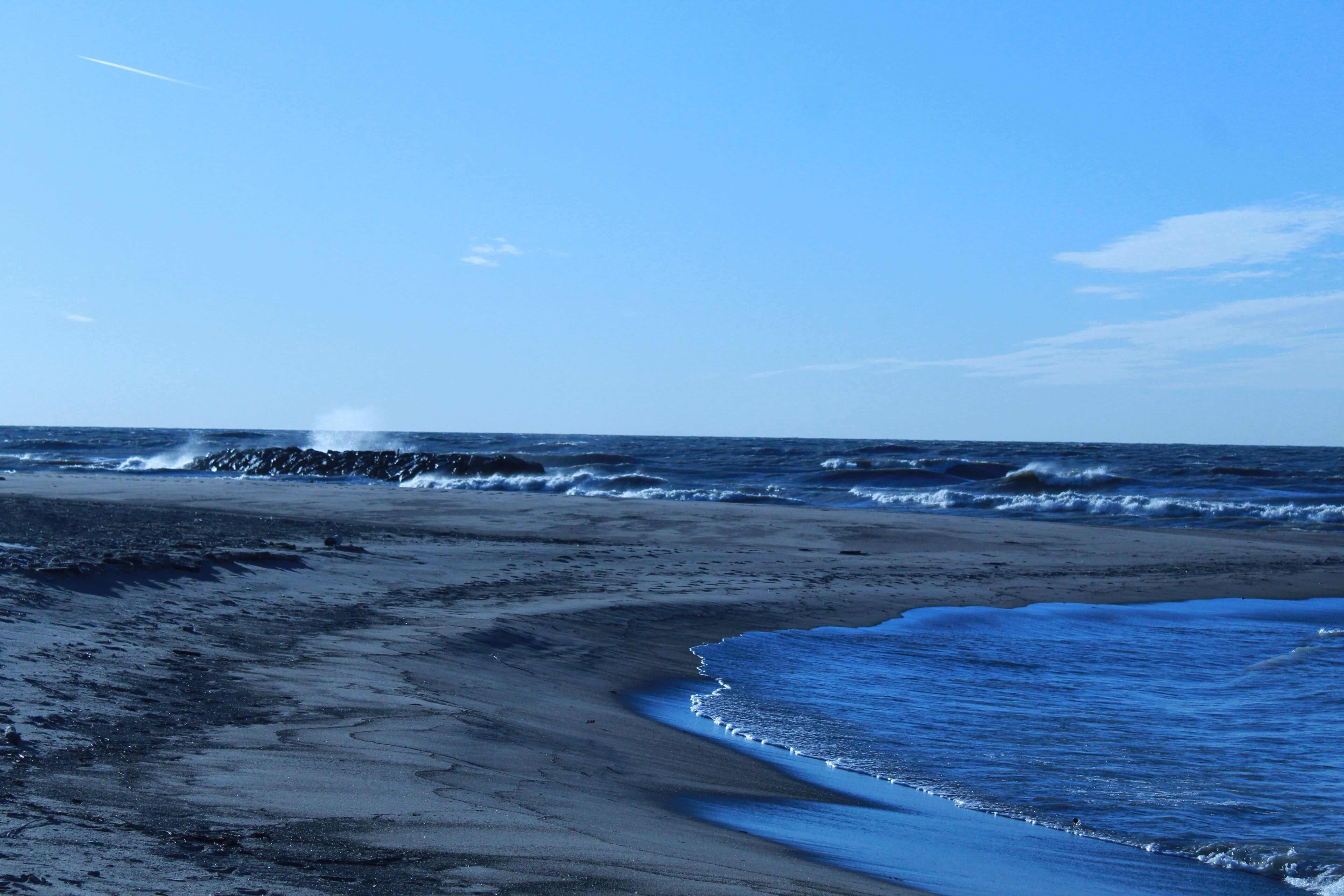 A sunny day as waves crash on rocks near a sandy beach on the shores of Lake Erie