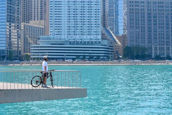 A bicyclist stops on a concrete overlook to gaze at bright turquoise water and downtown Chicago buildings