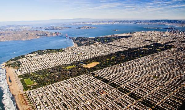 An aerial view of Golden Gate Park looking to the North and slightly East, with Ocean Beach to the left and both the Golden Gate Bridge and Bay Bridge visible in the distance