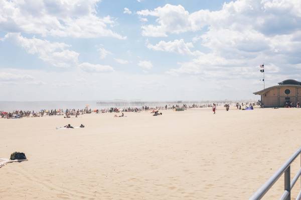 Bright sand and fluffy white clouds on a busy sunny day at Coney Island Beach in NYC
