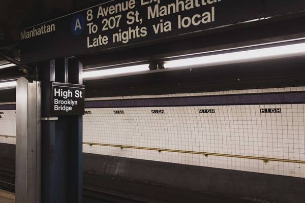 NYC High St Subway station featuring white square tiles and black accents, with signs for the Brooklyn Bridge
