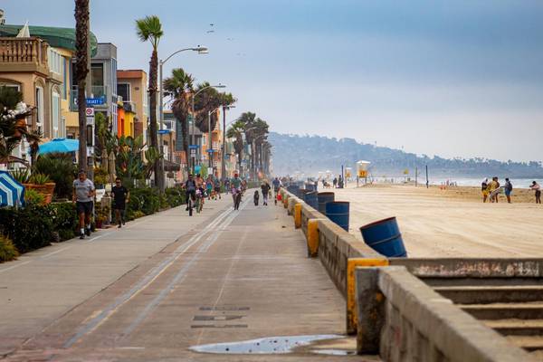 E-bikes and pedestrians share a multi-use path between colorful buildings and San Diego's Mission Beach