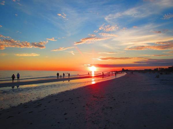 Visitors walk on Siesta Key Beach at sunset in Sarasota Florida with a red and orange horizon and peach colored clouds