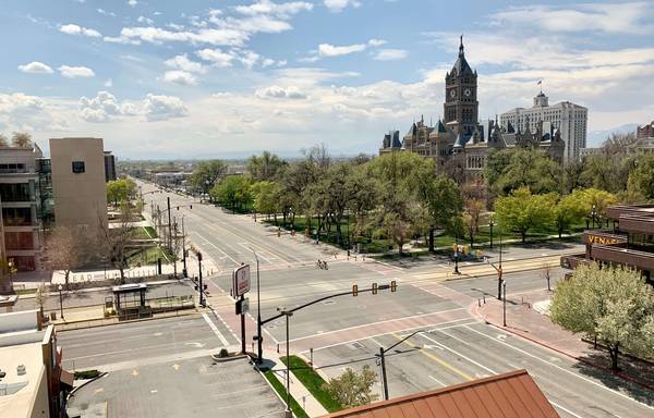 Green trees and gray concrete building at a large intersection under blue sky in Salt Lake City