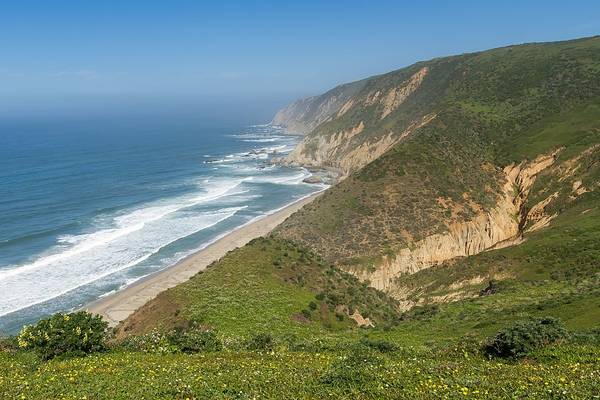 Ocean waves crash on a sandy beach below rolling green hills at Point Reyes National Seashore, where Class 1 e-bikes are permitted to ride