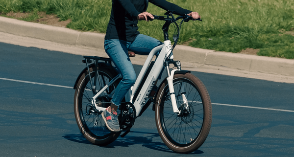 A rider shown from the waist down in black long-sleeve shirt, denim capris, and blue and red sneakers rides a white Magnum Metro X down an asphalt street with grass in the background