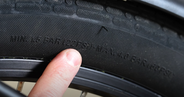 A finger points to the raised text showing tire pressure on the sidewall of an e-bike tire