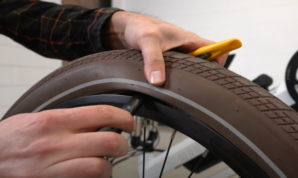 A hand works a tire lever in between the tire and rim of an e-bike wheel