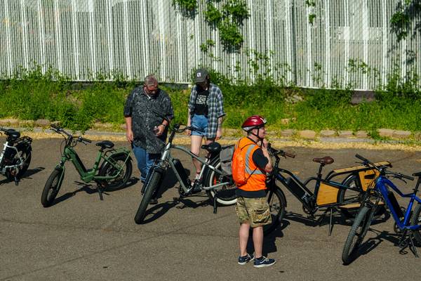 Attendees peruse a selection of parked e-bikes while one rider fastens his helmet to prepare for a test ride