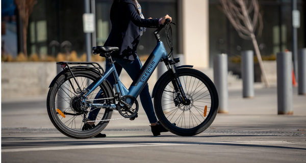 A rider in jeans and a black blazer walks their blue Magnum Cosmo X across a crosswalk in an urban environment
