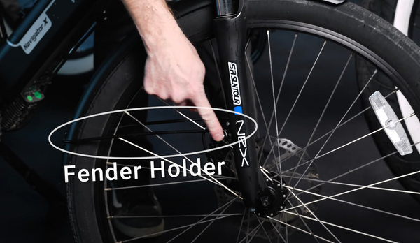 A hand points out the wire fender holder on an e-bike's fender, spanning between the fork and the fender