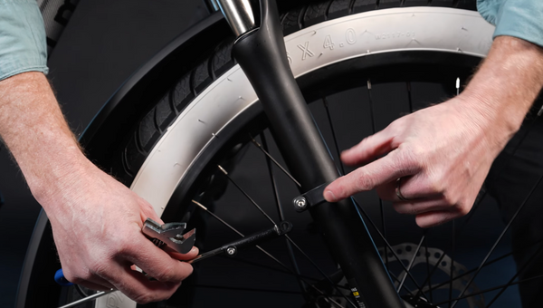 Hands hold the fender struct and point to the fender mount on the fork of a fat tire Ranger e-bike with white-wall tires