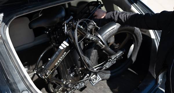 A person in a black jacket fits a black Magnum Premium 3 High Step folding e-bike into a black hatchback car.