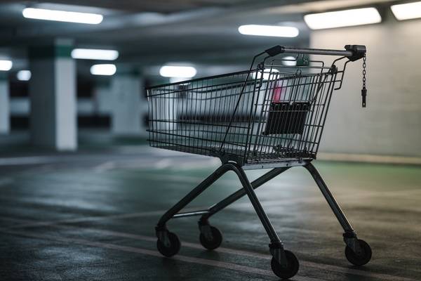 A black shopping cart in a dark empty parking garage with fluorescent lighting