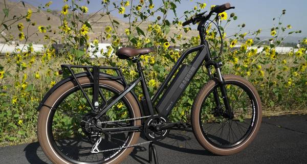 Black Magnum Metro S e-bike parked in front of a field of yellow flowers with power lines and bare hills in the background