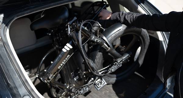 The Magnum Premium 3 folding e-bike in black, folded up, as a rider lifts it into the back of a black hatchback car