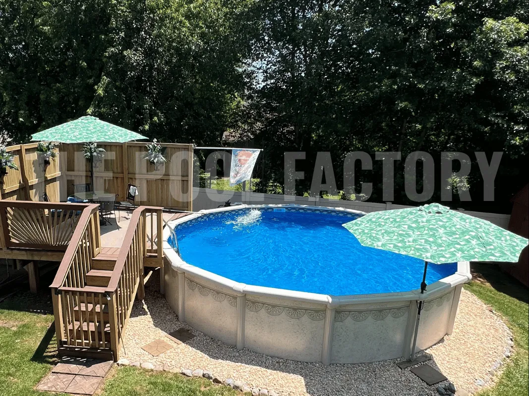 Round above ground pool with partial deck, grass border, and umbrella-covered seating