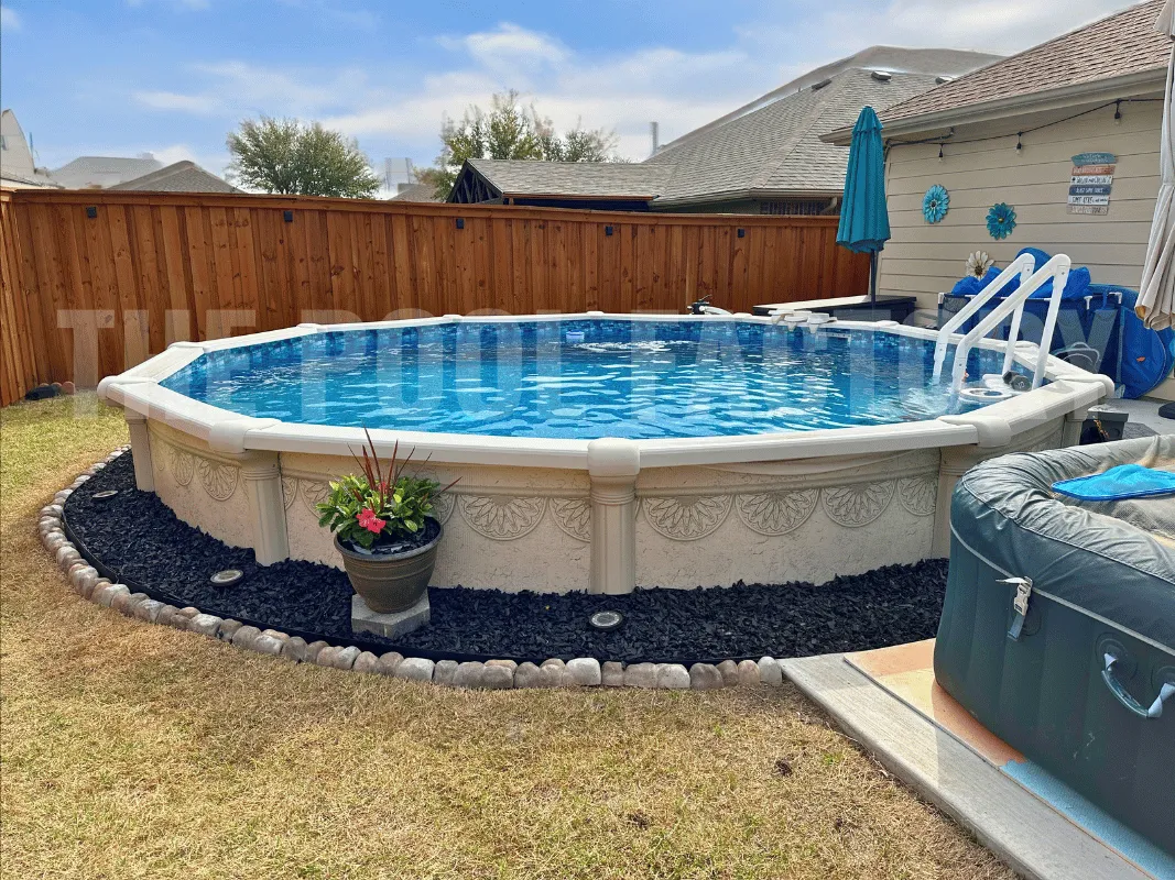 Round above ground swimming pool surrounded by grass, flower bed, and sunny skies