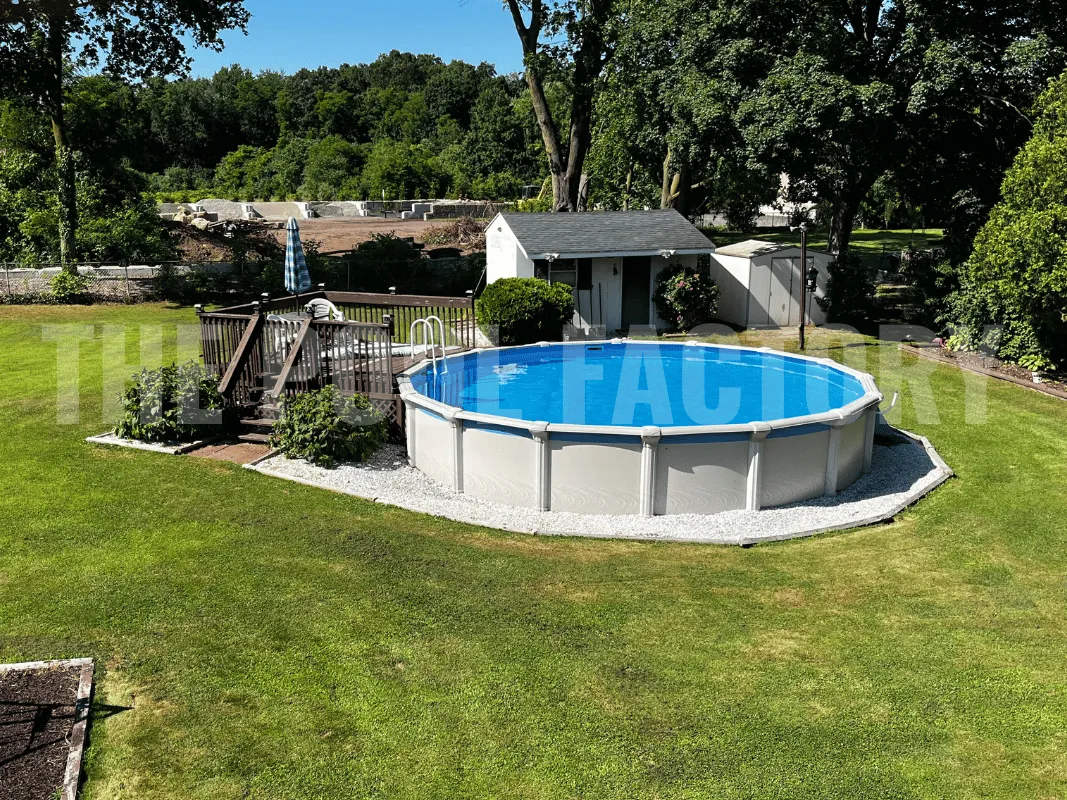 Round above ground pool with partial wooden deck, landscaped green grass, and decorative stone border
