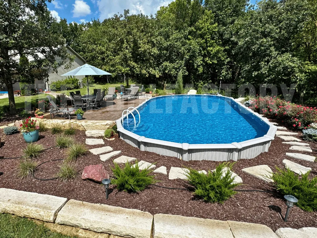 Modern backyard with semi-inground pool, stone patio area, decorative mulch, and blooming flowers