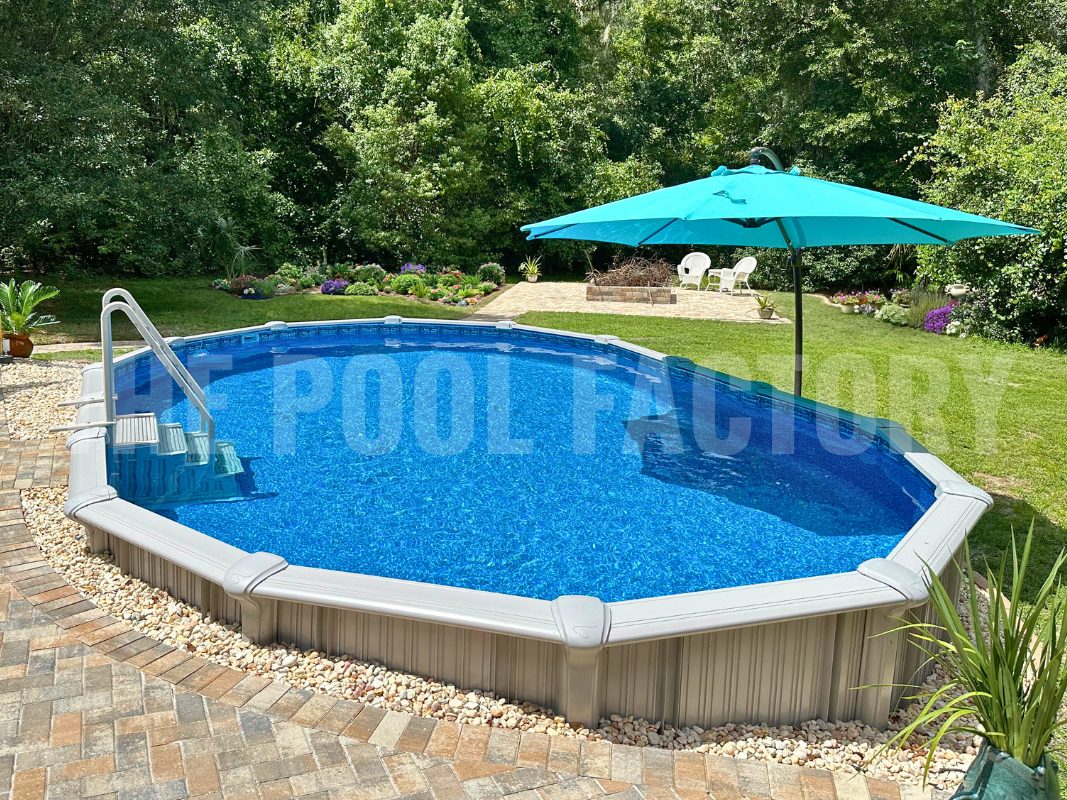 Semi-inground pool with stone patio, tall trees, and landscaping