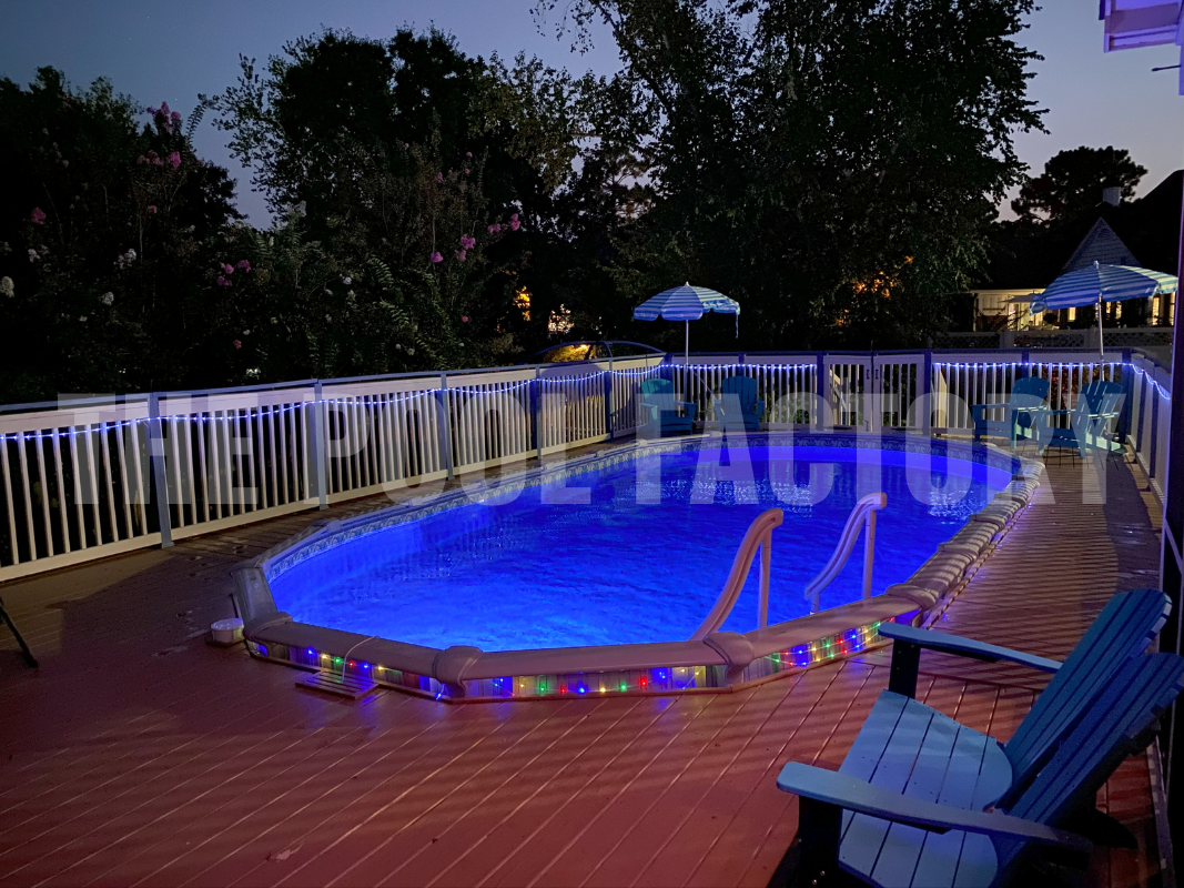 Oval swimming pool with full wrap around deck and night time lighting