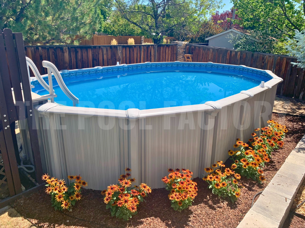 Oval above ground swimming pool surrounded by bright flowers, and a partial deck