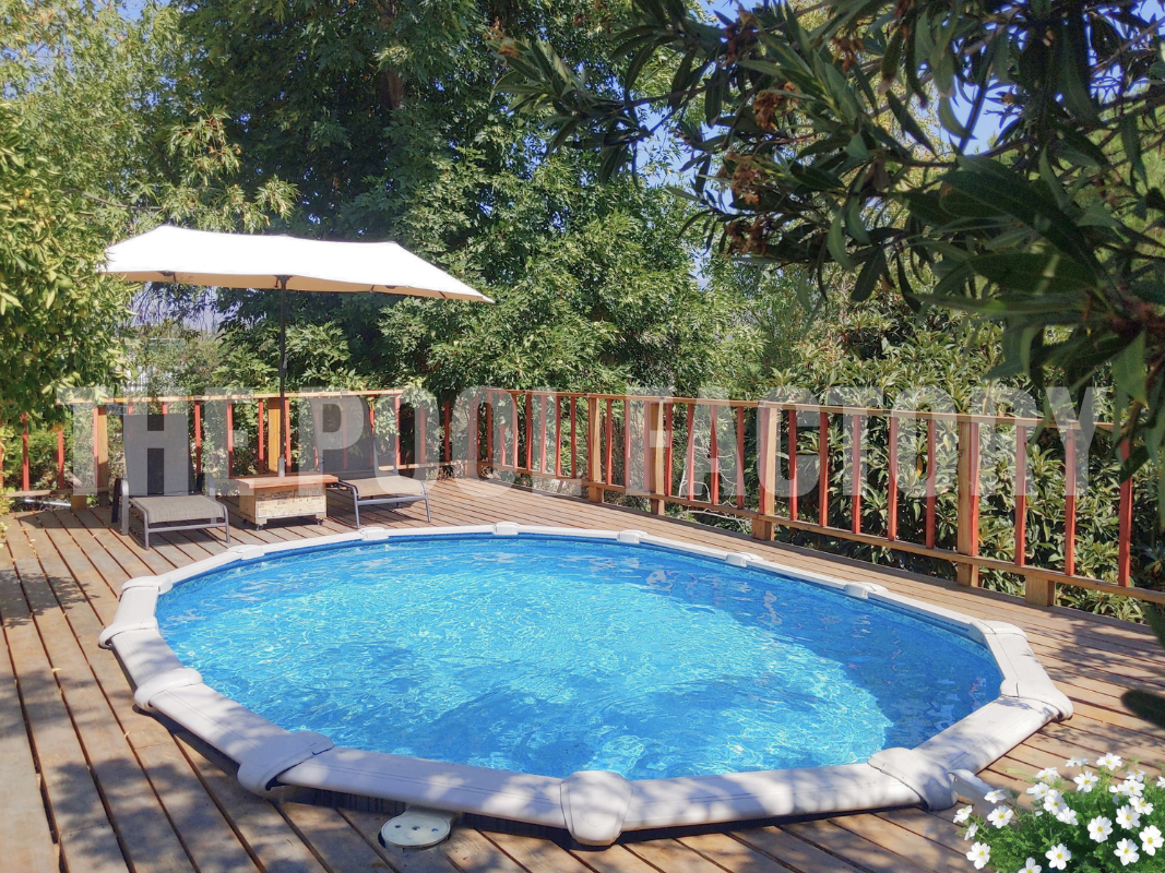 Backyard with oval swimming pool, sunny day, and full deck with lounge chairs