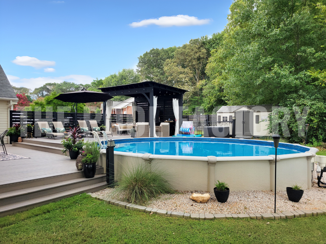 Backyard round semi inground pool with multi level deck, shrubs, and lush landscaping