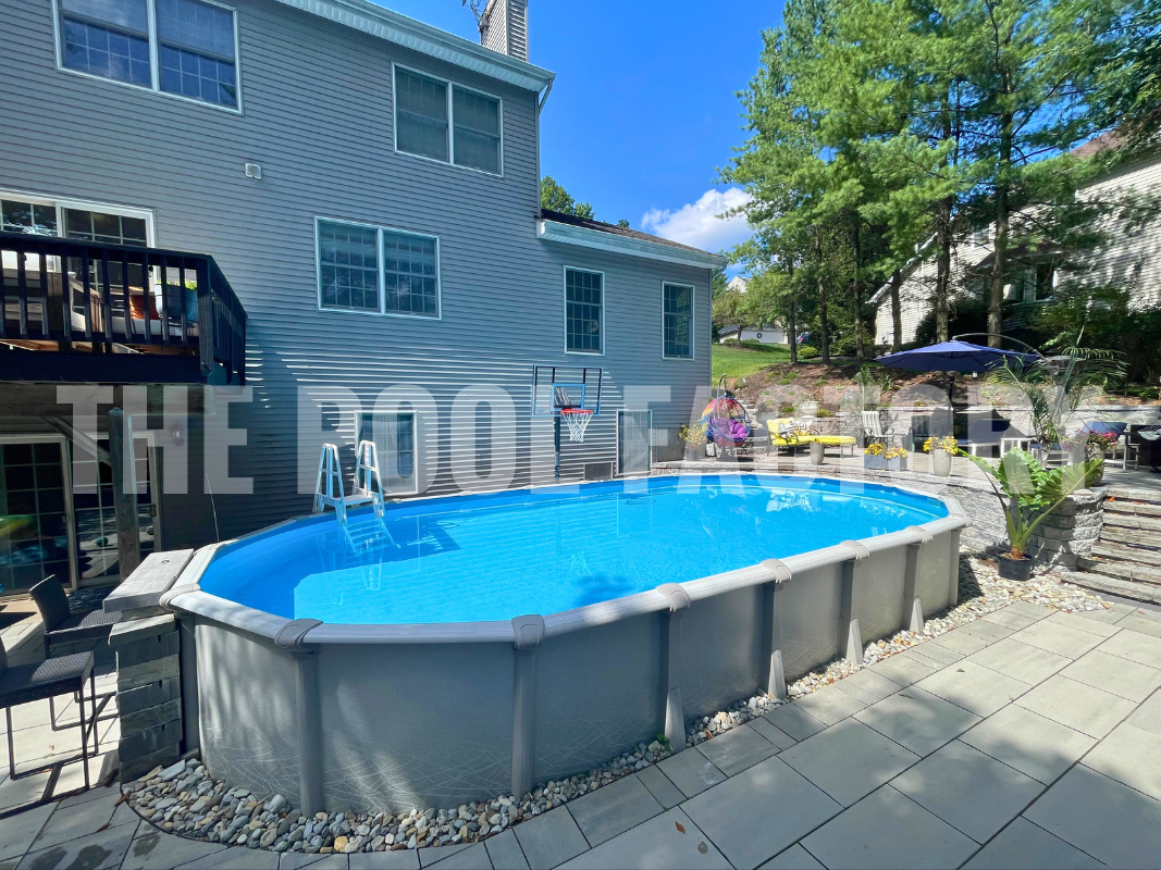 Oval saltwater swimming pool with stone patio, multi level stone work, plants, and bright sunshine