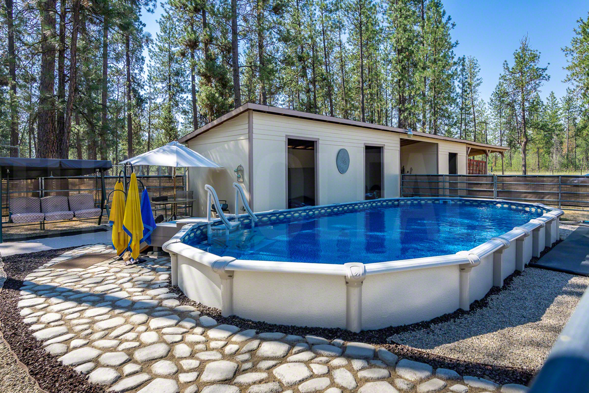 Oval saltwater semi-inground pool surrounded by tall trees and stone pathway