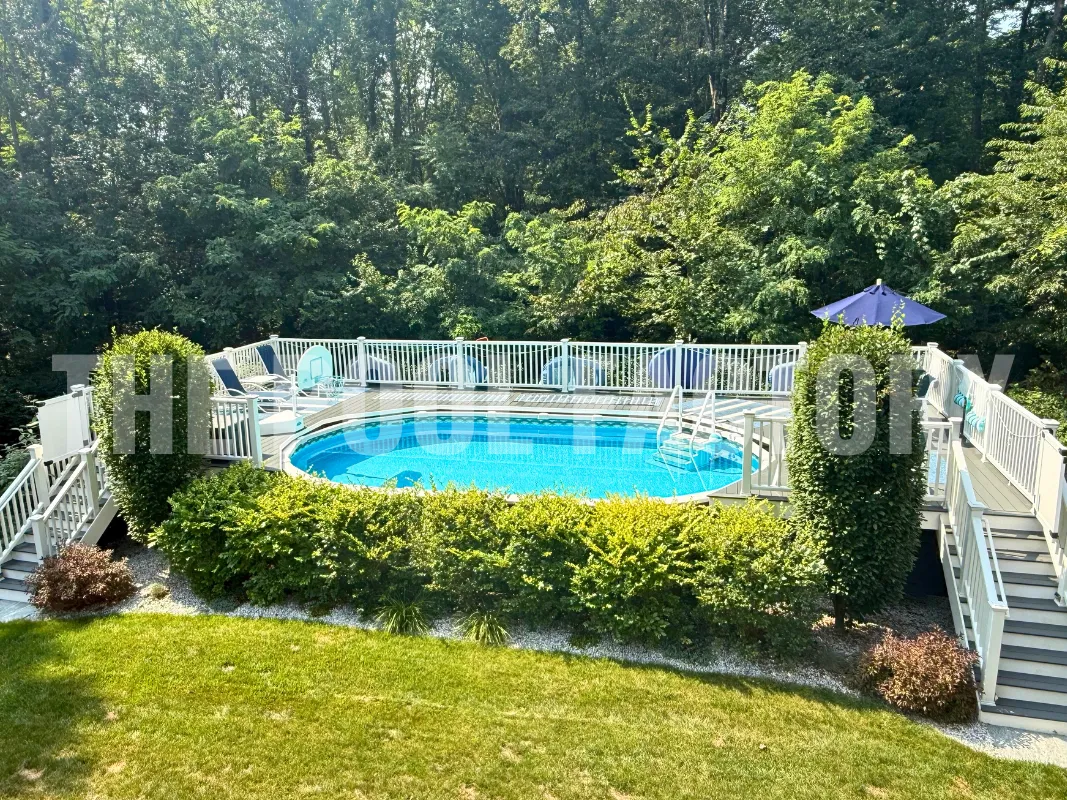 Oval backyard saltwater pool with grassy yard, two-entrance deck, and lush shrubbery