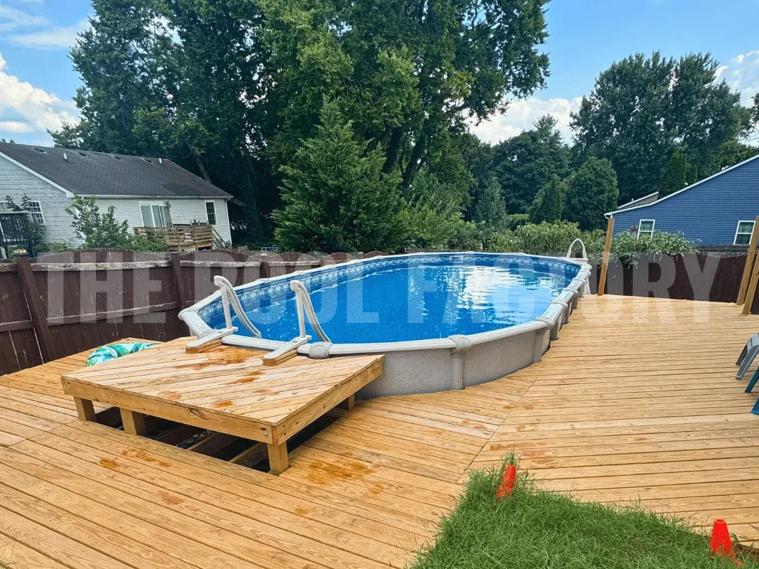 Oval above ground swimming pool with full wraparound deck and green hedges