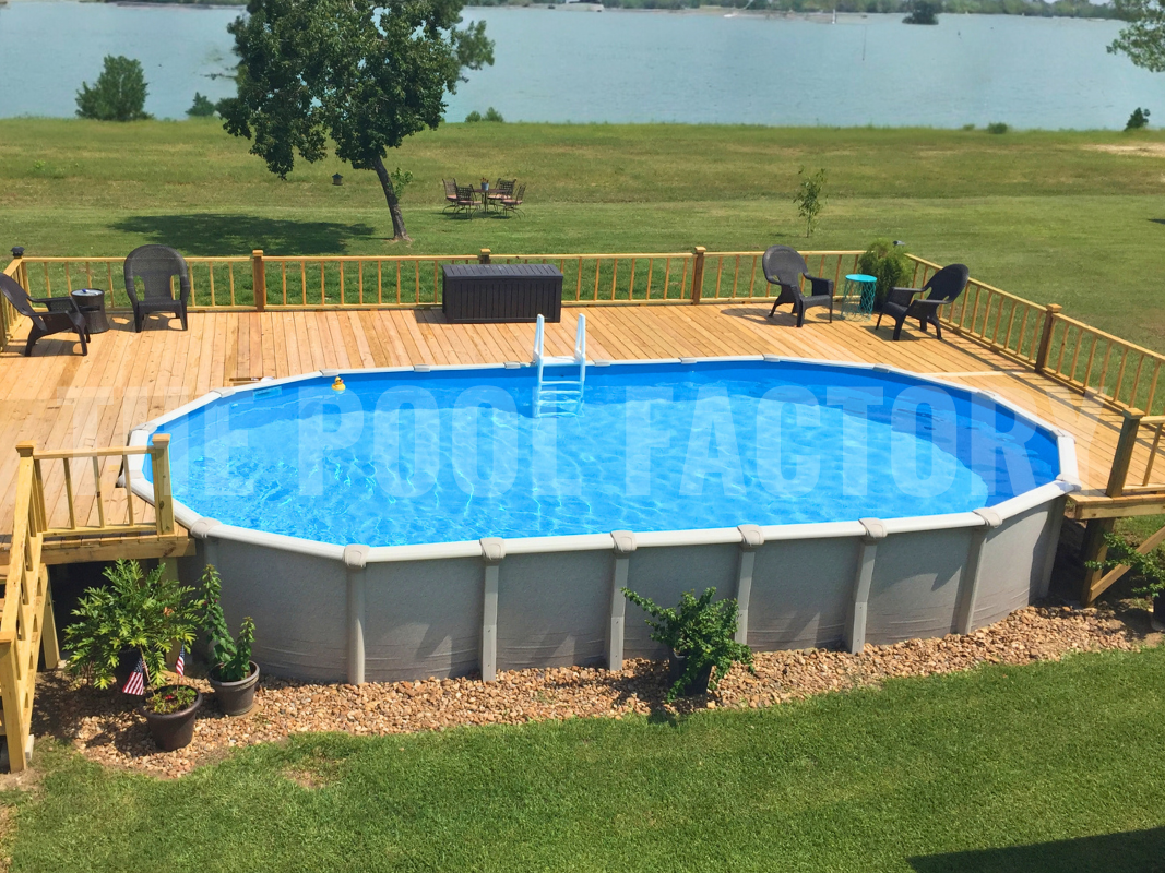 Above ground oval swimming pool with large deck, trees, and lake backdrop