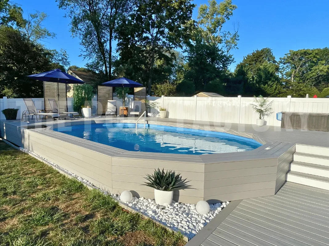 Oval above ground pool featuring grey deck, white vinyl fence, and grass & gravel landscaping