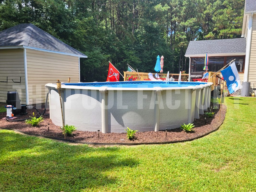 Oval above ground swimming pool surrounded by neatly cut grass and tall trees