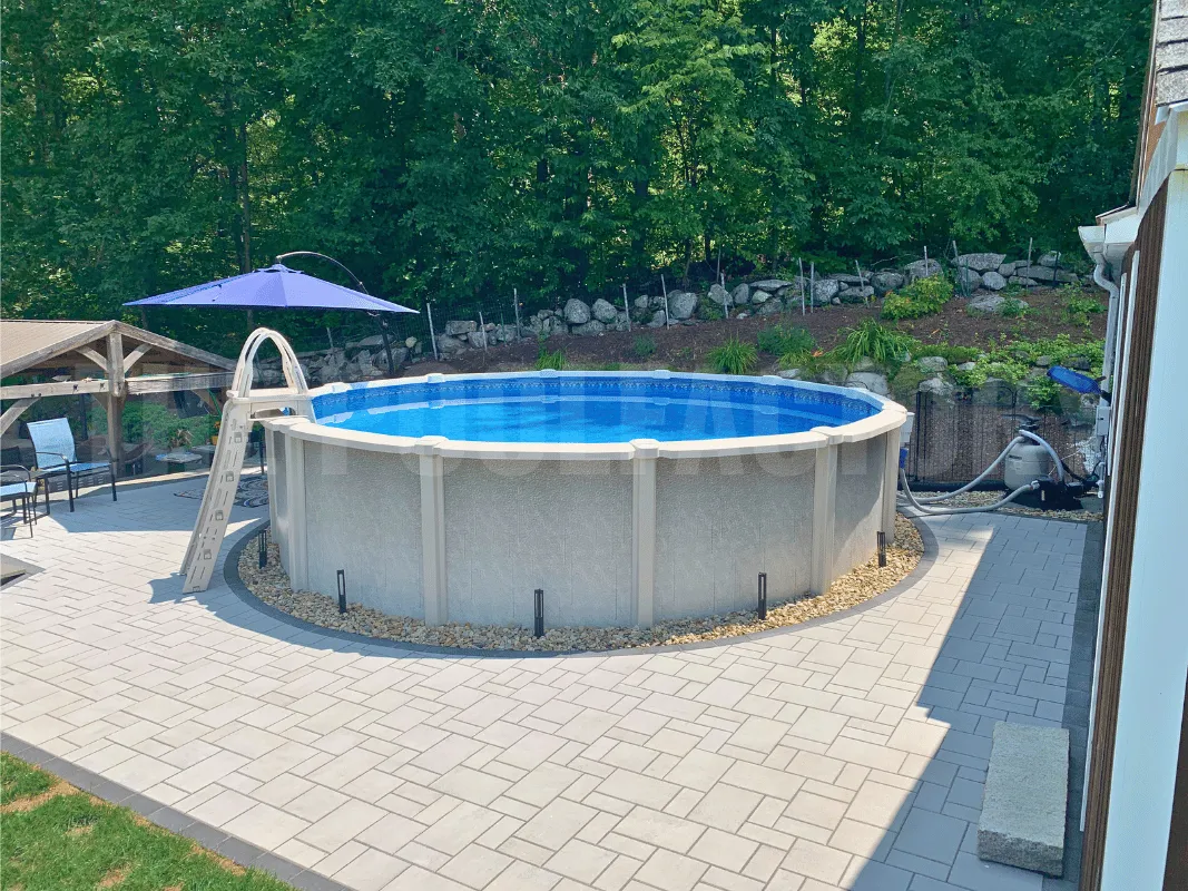 Round above ground saltwater pool with paver patio and backyard shrubs