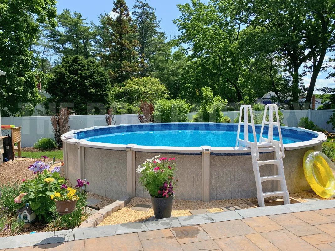 Round above ground saltwater pool with paver patio surrounded by colorful flowers, green grass, and garden landscaping