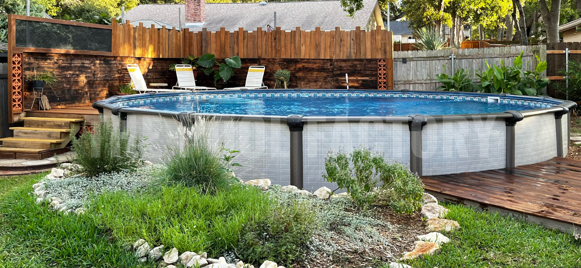 Round semi inground pool with deck access and shrubs on a sunny day