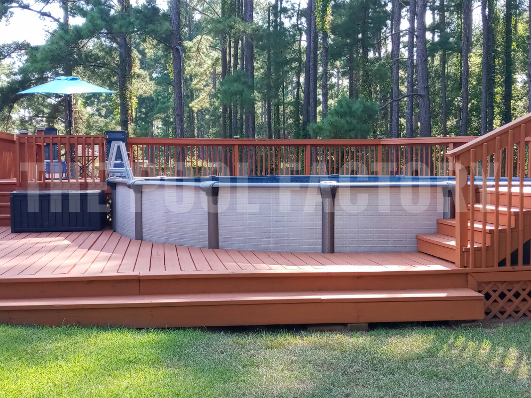 Above ground swimming pool with deck, steps, and tall trees