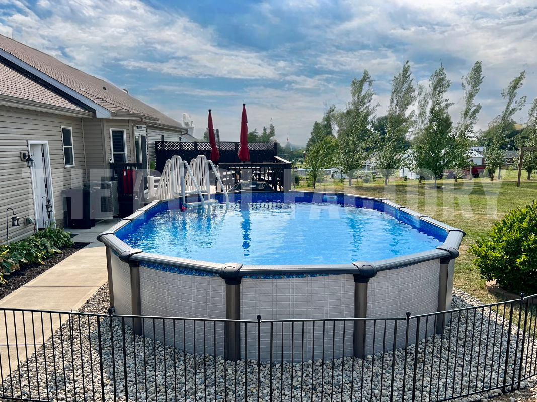 Oval above ground pool surrounded by tall trees and decorative rocks