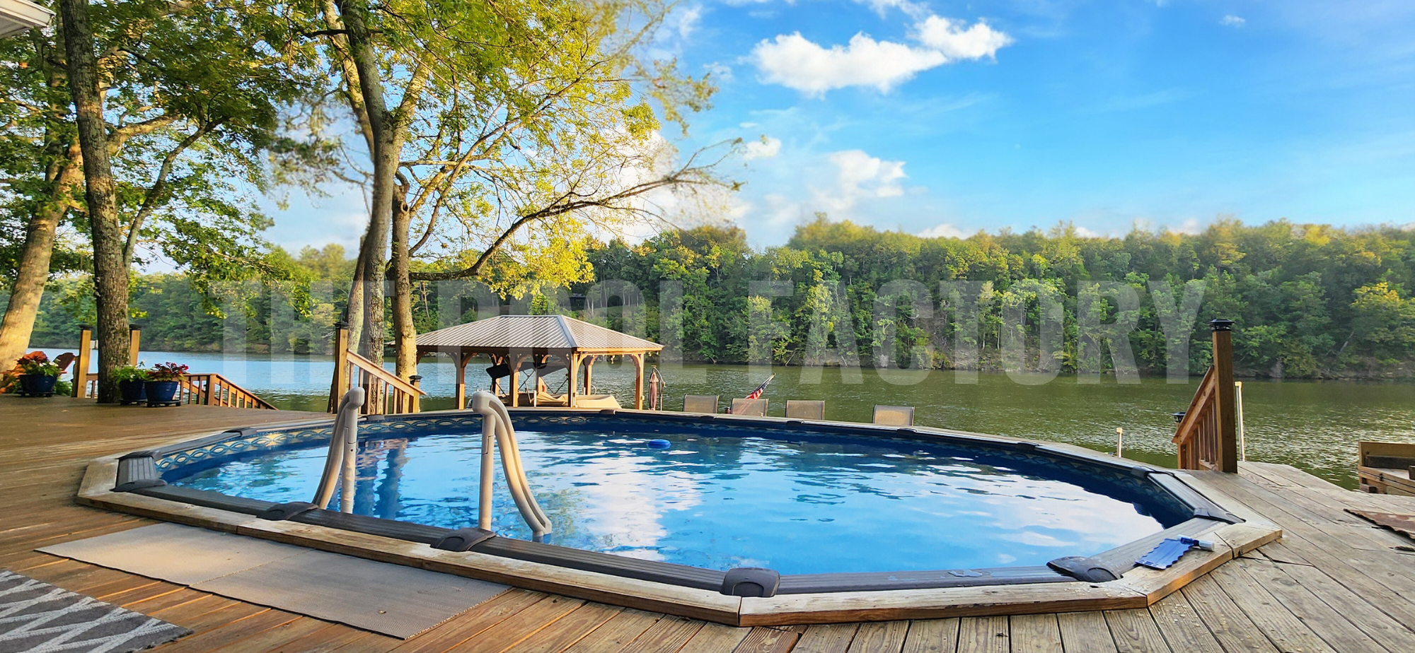 Oval swimming pool with deck access, trees, and lake view