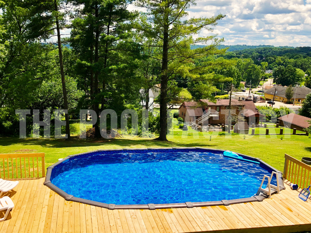 Oval swimming pool with partial deck, tall trees, and sunny hill view