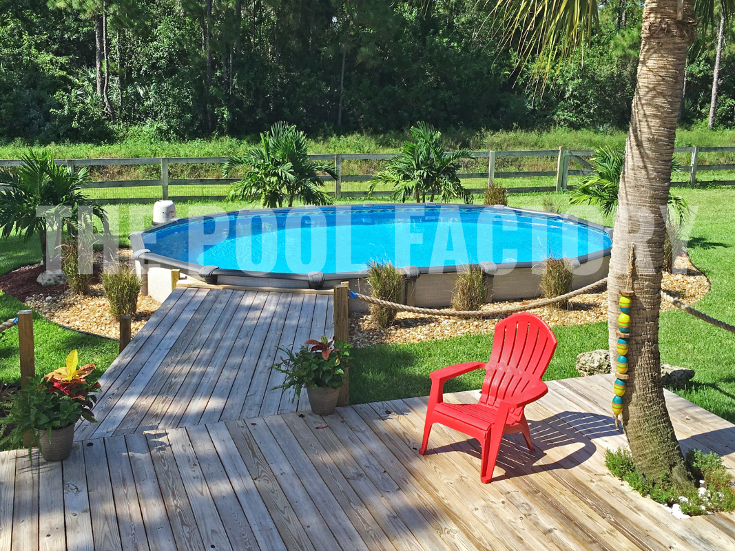 Oval swimming pool with deck, comfortable seating, and forest backdrop on a sunny day