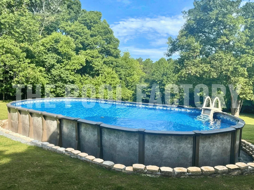 Oval above ground swimming pool with stone paver retaining wall and tree lined backyard